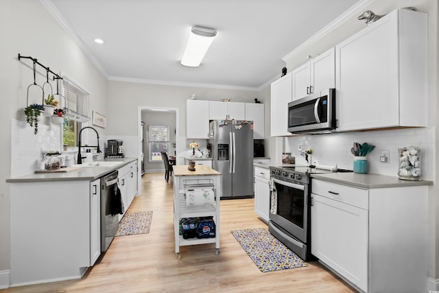 kitchen featuring white cabinets, sink, light hardwood / wood-style flooring, ornamental molding, and appliances with stainless steel finishes