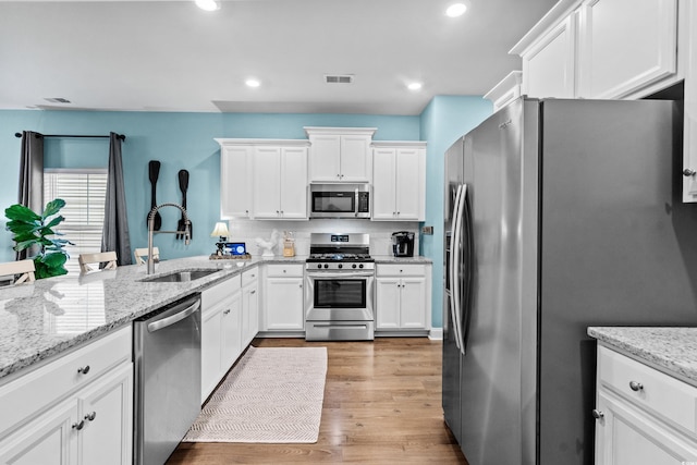 kitchen featuring sink, light stone countertops, light wood-type flooring, white cabinetry, and stainless steel appliances