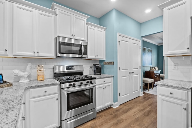 kitchen with white cabinets, backsplash, wood-type flooring, and stainless steel appliances