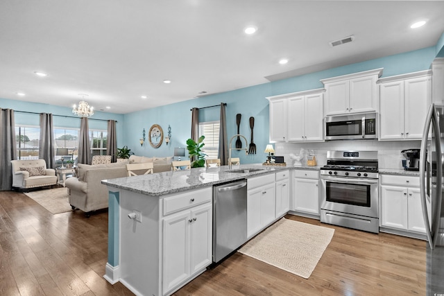 kitchen featuring kitchen peninsula, light wood-type flooring, stainless steel appliances, sink, and white cabinetry