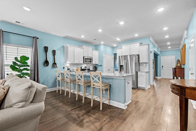 kitchen with a breakfast bar area, light hardwood / wood-style floors, light stone counters, white cabinetry, and stainless steel appliances