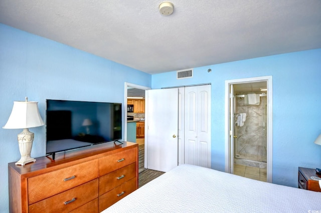 bedroom with a textured ceiling, connected bathroom, hardwood / wood-style flooring, and a closet