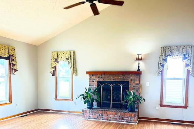 living room with a brick fireplace, a textured ceiling, vaulted ceiling, ceiling fan, and hardwood / wood-style floors