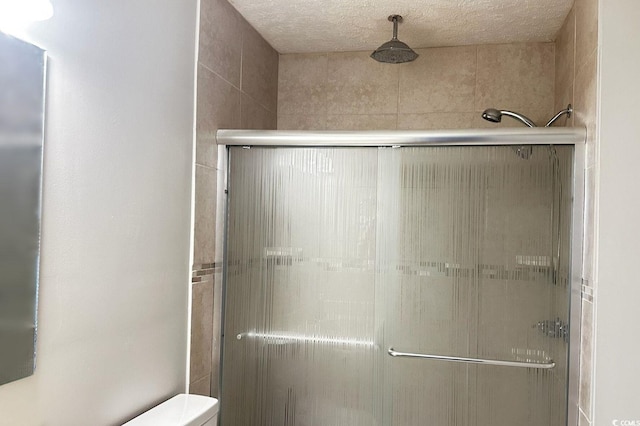 bathroom featuring a shower with door, a textured ceiling, and toilet