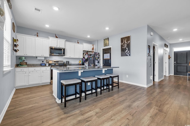 kitchen featuring white cabinetry, stainless steel appliances, dark stone countertops, a kitchen island with sink, and light wood-type flooring