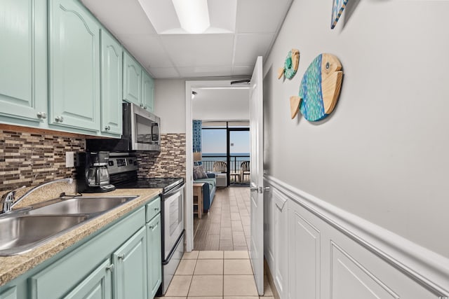 kitchen featuring sink, backsplash, appliances with stainless steel finishes, light tile patterned flooring, and green cabinetry