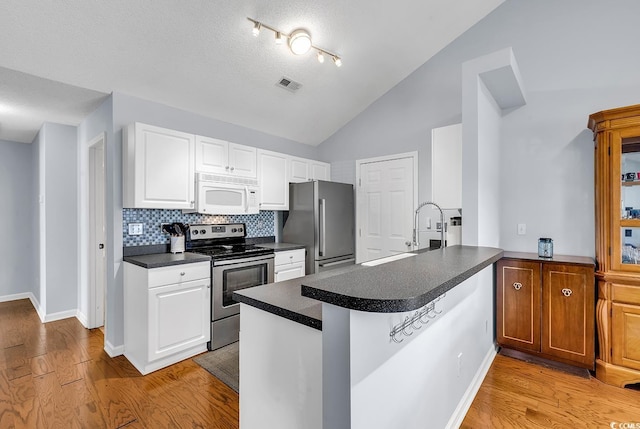 kitchen featuring backsplash, white cabinets, vaulted ceiling, kitchen peninsula, and stainless steel appliances