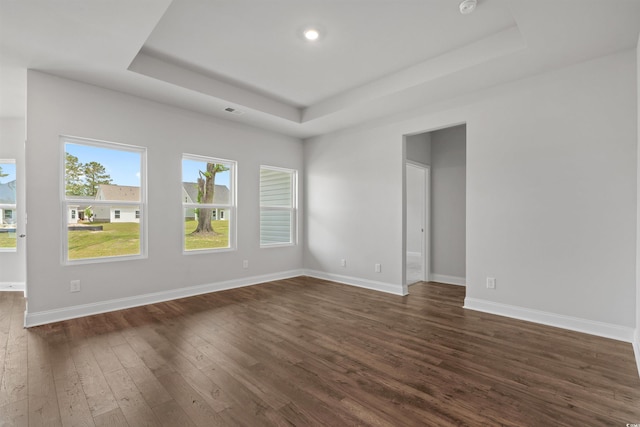 spare room with baseboards, visible vents, dark wood-style flooring, and a tray ceiling