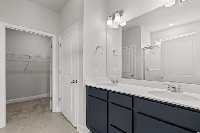 bathroom with double vanity, a walk in closet, a stall shower, and a sink