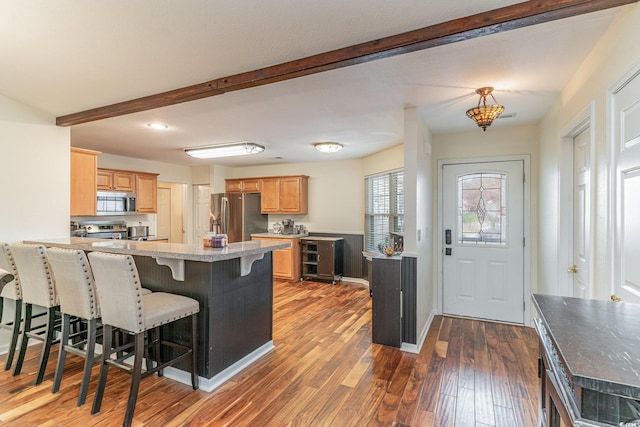 kitchen featuring a kitchen breakfast bar, dark hardwood / wood-style floors, kitchen peninsula, light brown cabinetry, and appliances with stainless steel finishes