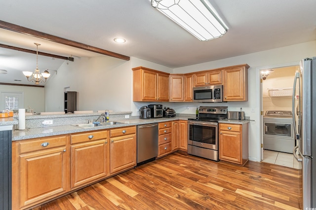 kitchen featuring appliances with stainless steel finishes, sink, an inviting chandelier, hardwood / wood-style floors, and washer / clothes dryer