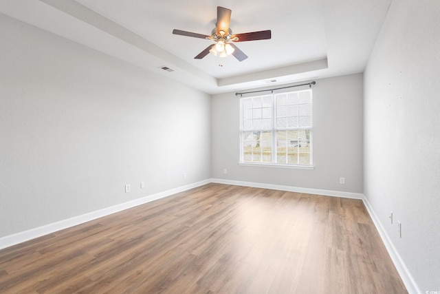 unfurnished room with a raised ceiling, ceiling fan, and hardwood / wood-style flooring