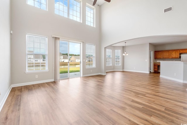 unfurnished living room with a healthy amount of sunlight, light wood-type flooring, and a high ceiling