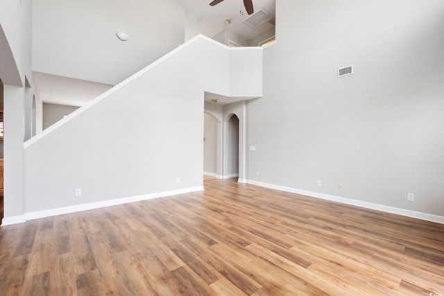 unfurnished living room featuring light wood-type flooring, a towering ceiling, and ceiling fan