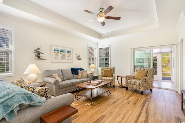 living room featuring ceiling fan, light wood-type flooring, crown molding, and a tray ceiling