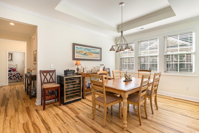 dining space with a raised ceiling, light wood-type flooring, ornamental molding, and wine cooler