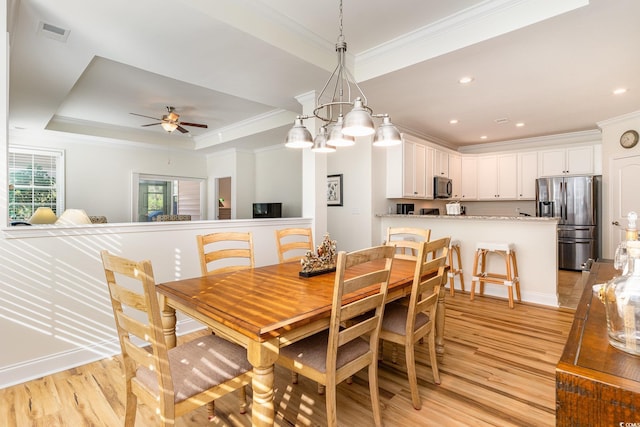 dining space with ceiling fan with notable chandelier, light hardwood / wood-style floors, crown molding, and a tray ceiling