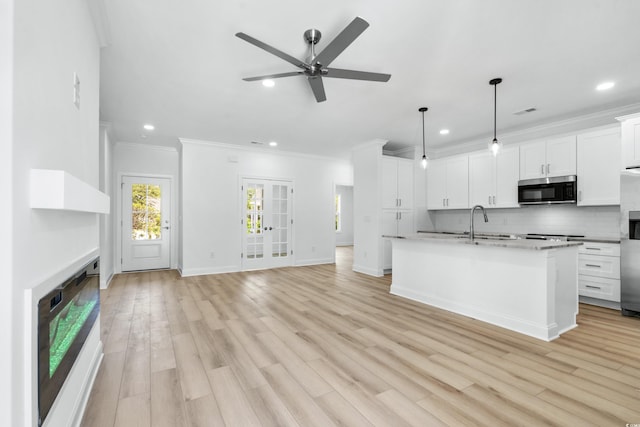 kitchen with white cabinets, a center island with sink, ceiling fan, decorative light fixtures, and stainless steel appliances