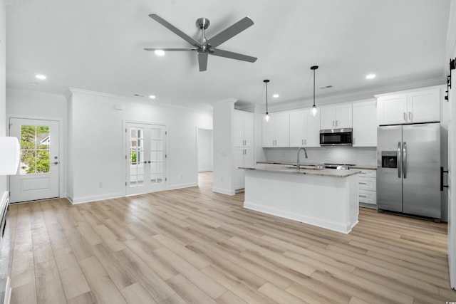 kitchen featuring a center island with sink, white cabinets, stainless steel appliances, and decorative light fixtures