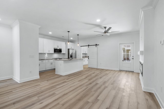 kitchen featuring a kitchen island with sink, white cabinets, a barn door, decorative light fixtures, and stainless steel appliances