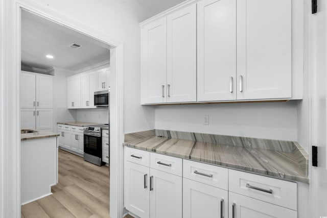 kitchen with white cabinets, light hardwood / wood-style floors, light stone counters, and appliances with stainless steel finishes