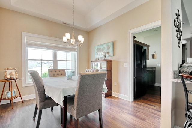 dining room with a chandelier, hardwood / wood-style floors, and a raised ceiling