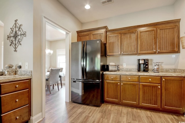 kitchen with light wood-type flooring, stainless steel refrigerator, and an inviting chandelier