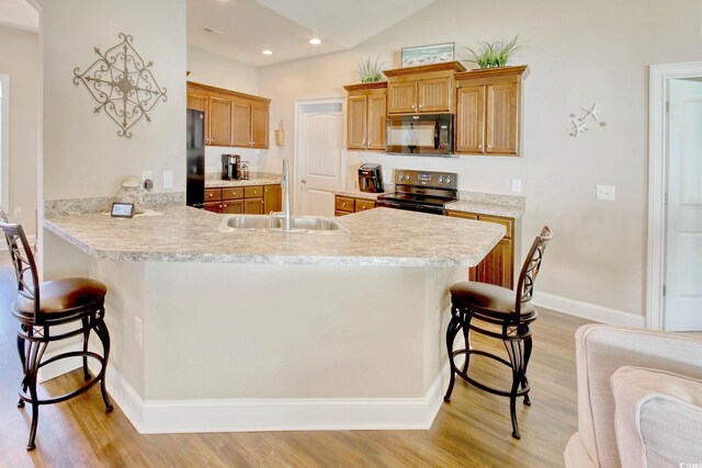 kitchen with kitchen peninsula, light hardwood / wood-style floors, a breakfast bar area, and black appliances