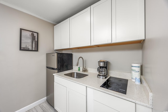 kitchen featuring black electric cooktop, white cabinets, stainless steel refrigerator, light stone counters, and sink