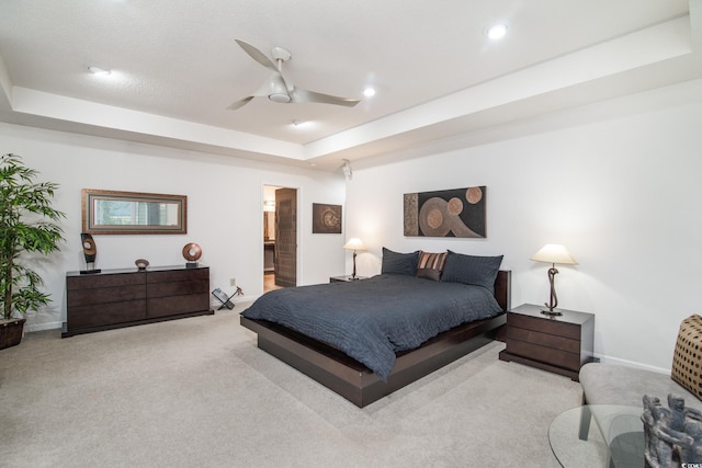 bedroom with ceiling fan, a raised ceiling, ensuite bathroom, and light carpet