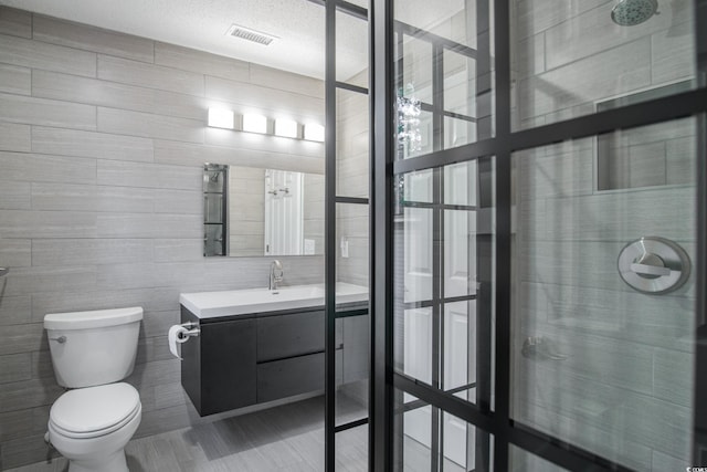 bathroom with a shower, vanity, toilet, and tile walls