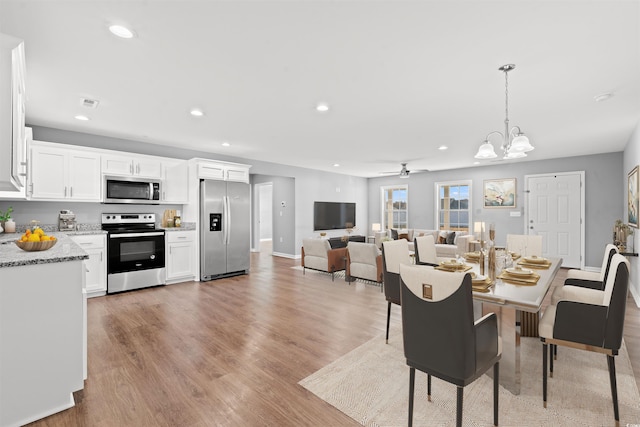 dining space featuring ceiling fan with notable chandelier and light hardwood / wood-style flooring