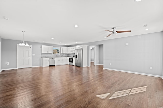 unfurnished living room featuring ceiling fan with notable chandelier and dark wood-type flooring