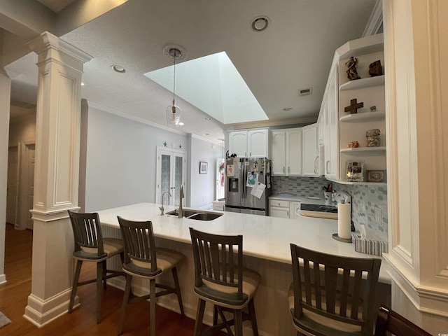 kitchen featuring open shelves, stainless steel fridge, a sink, a peninsula, and ornate columns