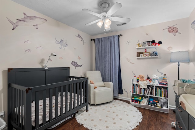 bedroom with ceiling fan, a nursery area, and dark hardwood / wood-style floors