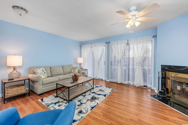 living room featuring ceiling fan, a high end fireplace, a textured ceiling, and light wood-type flooring