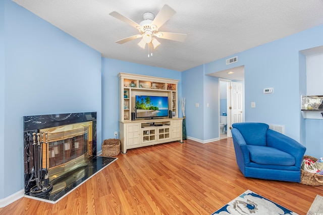 living room featuring ceiling fan, wood-type flooring, a textured ceiling, and a premium fireplace