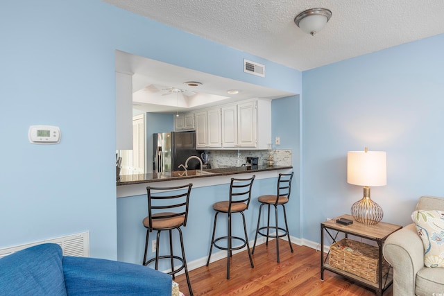 kitchen with hardwood / wood-style floors, backsplash, kitchen peninsula, white cabinetry, and stainless steel fridge with ice dispenser