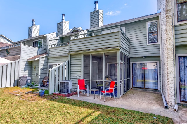 rear view of property with a lawn, a sunroom, central air condition unit, a balcony, and a patio area