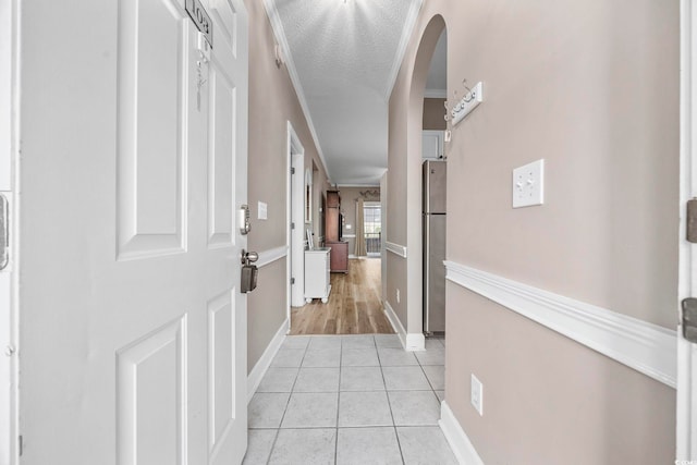 corridor with a textured ceiling, light tile patterned floors, and ornamental molding