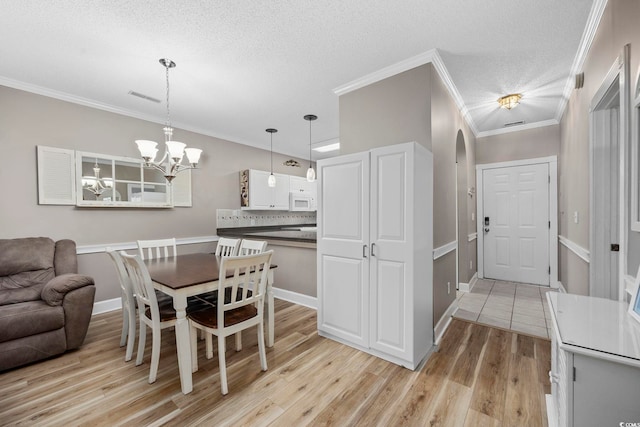 dining space with crown molding, light hardwood / wood-style flooring, a textured ceiling, and a notable chandelier