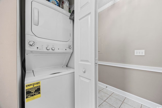 laundry room featuring light tile patterned floors, stacked washer and dryer, and ornamental molding