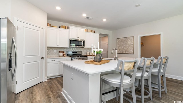 kitchen with dark hardwood / wood-style floors, appliances with stainless steel finishes, white cabinetry, and an island with sink