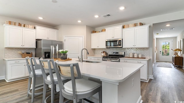 kitchen with a center island with sink, sink, white cabinetry, appliances with stainless steel finishes, and a kitchen breakfast bar