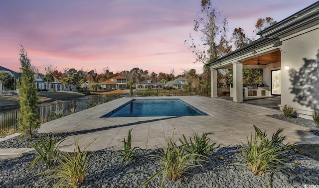 pool at dusk with area for grilling and a patio