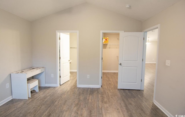 unfurnished bedroom featuring lofted ceiling, a walk in closet, a closet, and dark wood-type flooring