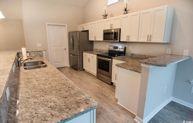 kitchen with kitchen peninsula, stainless steel appliances, sink, dark stone countertops, and white cabinetry