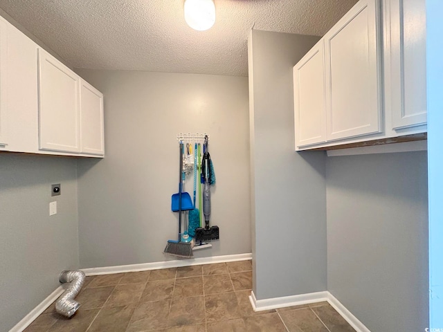 washroom with electric dryer hookup, dark tile patterned floors, cabinets, and a textured ceiling