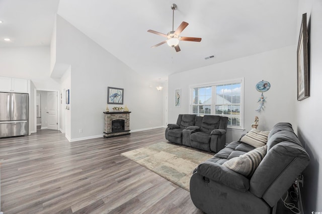 living room featuring hardwood / wood-style floors, a fireplace, high vaulted ceiling, and ceiling fan