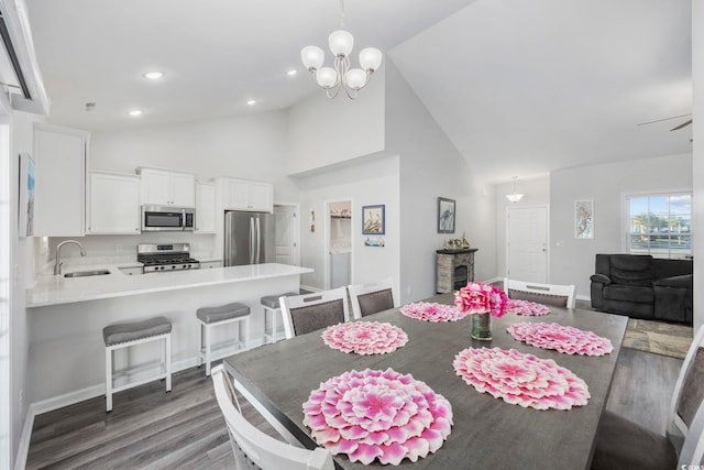 dining room featuring ceiling fan with notable chandelier, sink, dark wood-type flooring, and high vaulted ceiling